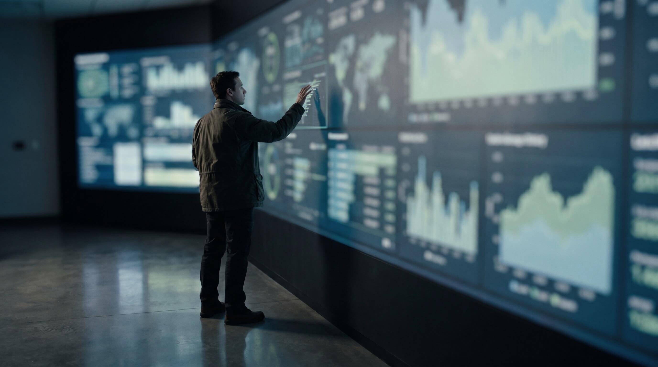 An analyst at a wall of large data screens with charts and a world map