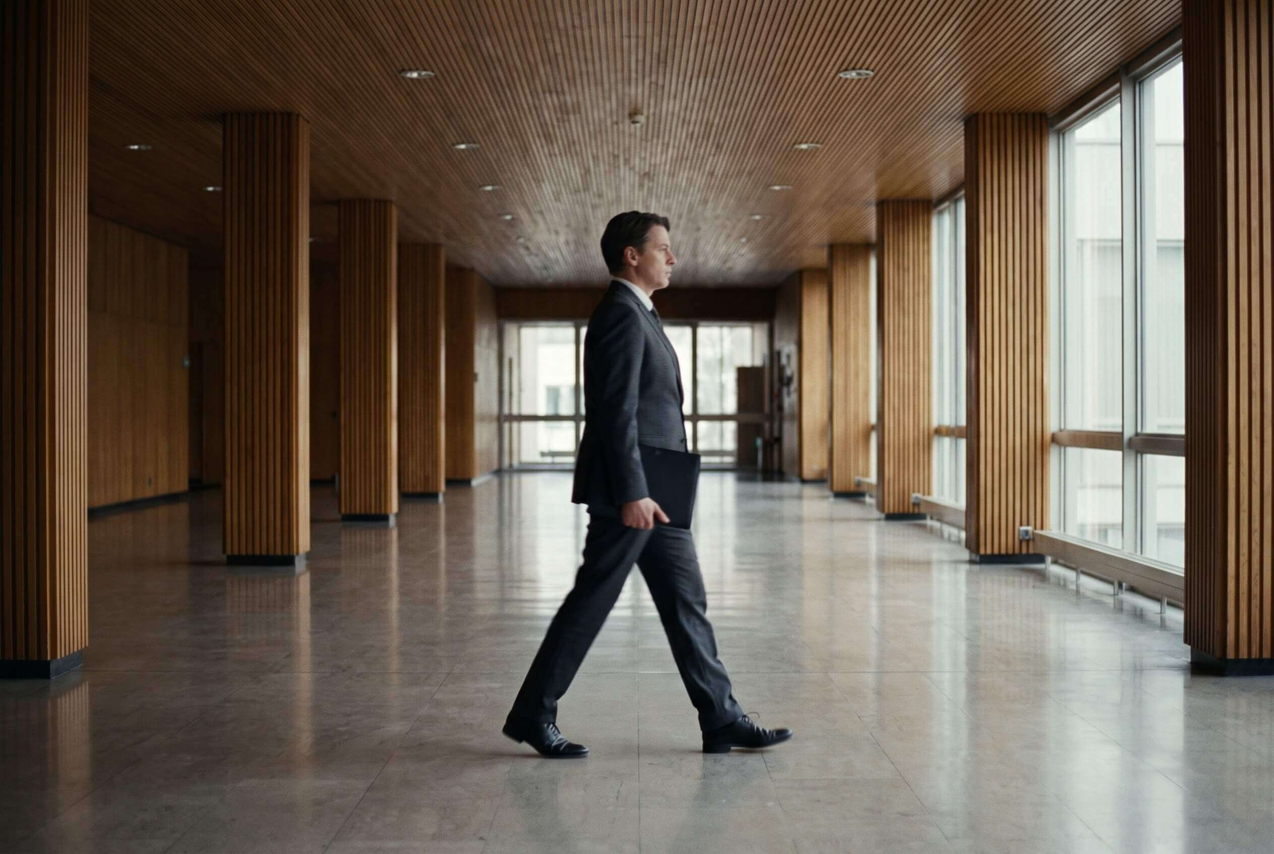 A man in a suit walking along a long wood-panelled corridor of a courthouse